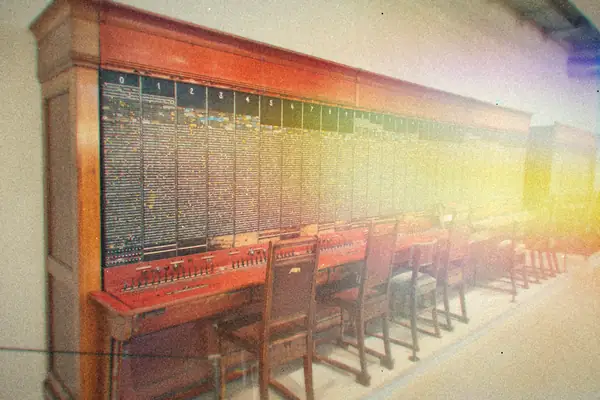 A long wooden telephone switchboard with rows of operator chairs in a museum hall.