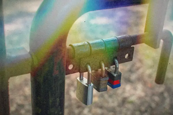 A rusty metal gate latch locked shut with three padlocks.