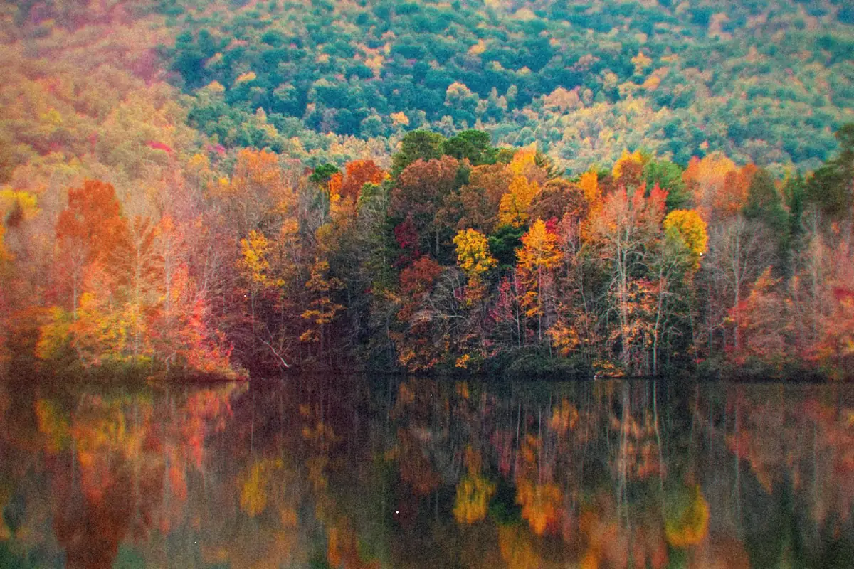 A lake reflecting a hillside of red, orange and yellow autumn trees.