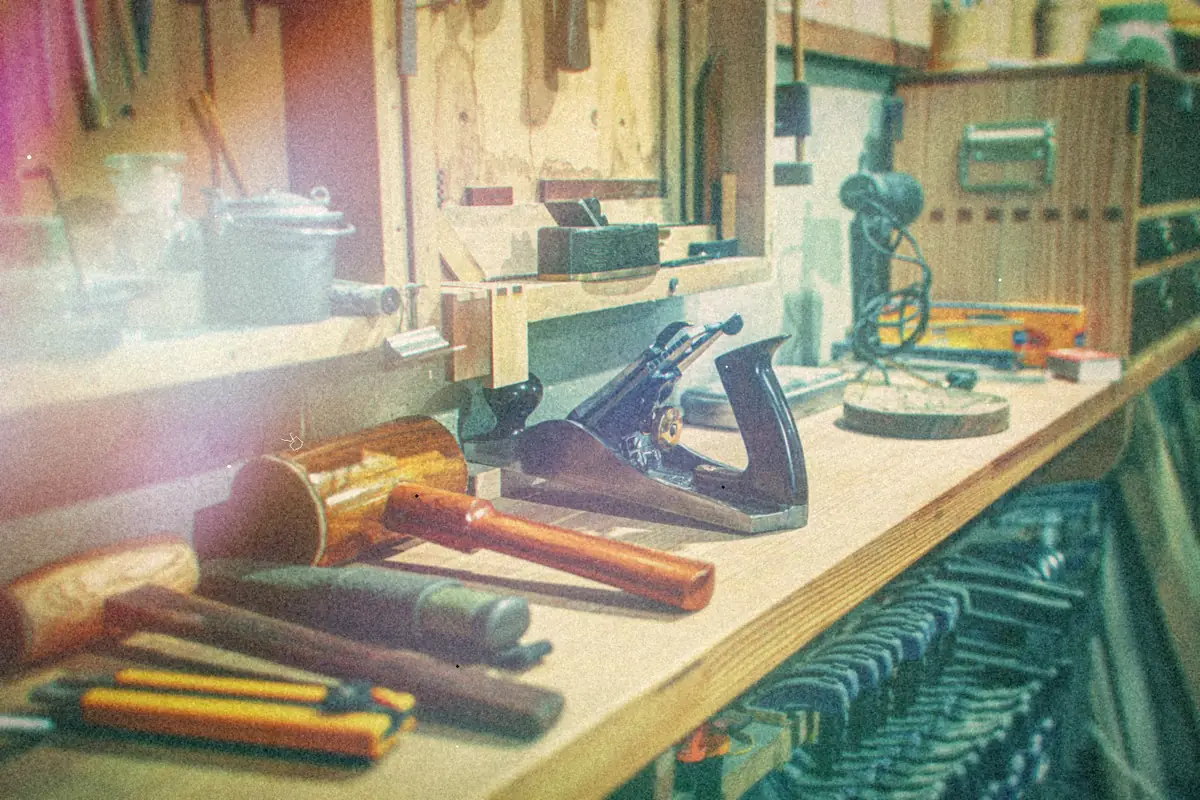 A wooden workbench with hammers, a hand plane and clamps in a tidy workshop.