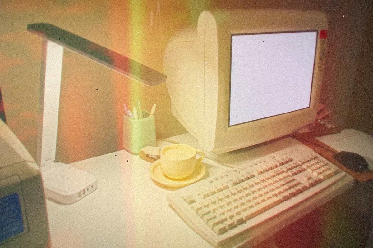 A beige CRT computer and keyboard on a desk beside a coffee cup and a pencil cup.