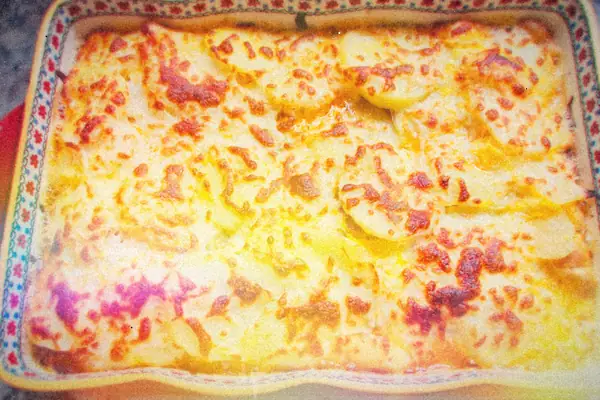 A golden, bubbly baked potato and cheese casserole in a patterned baking dish.