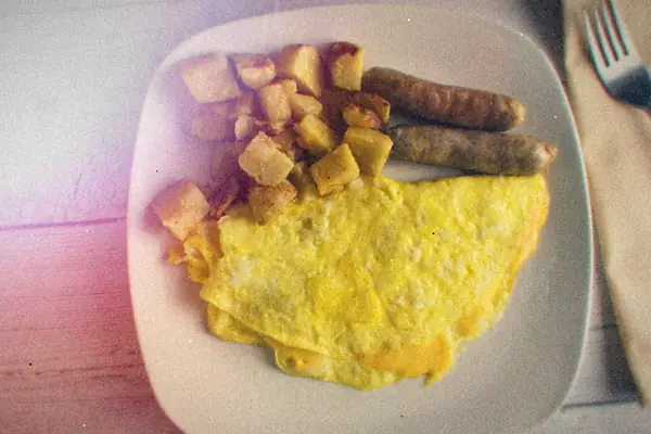 A plate with a folded omelet, browned potato cubes and two sausages.