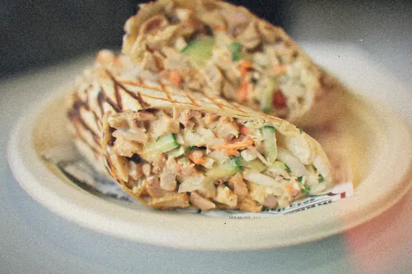 A grilled chicken salad wrap cut in half on a white plate.