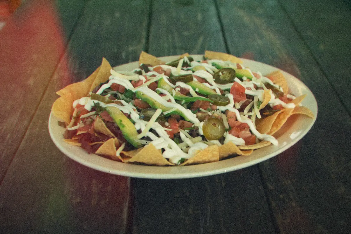 A platter of beef nachos with avocado, tomatoes, jalapenos and a drizzle of sour cream.