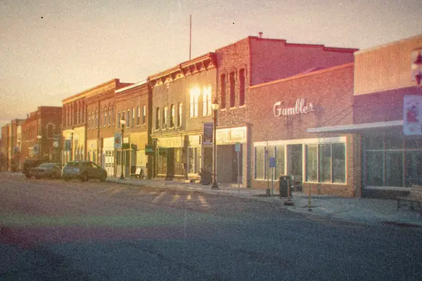 A quiet small-town main street of brick storefronts at sunset.