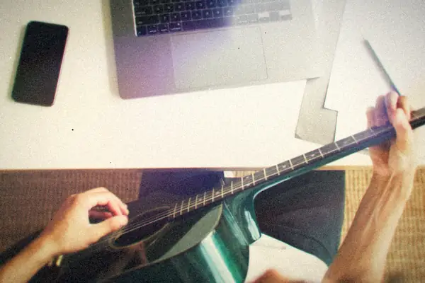 A desk with an acoustic guitar, a laptop and handwritten music.