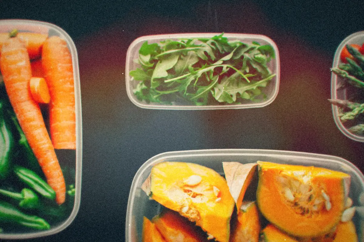 Clear plastic storage containers holding carrots, peppers, arugula, asparagus and cut squash.