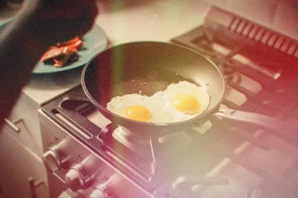 Two eggs frying sunny side up in a pan on a gas stove.