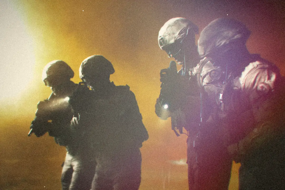 Four soldiers in tactical gear advancing through smoke.