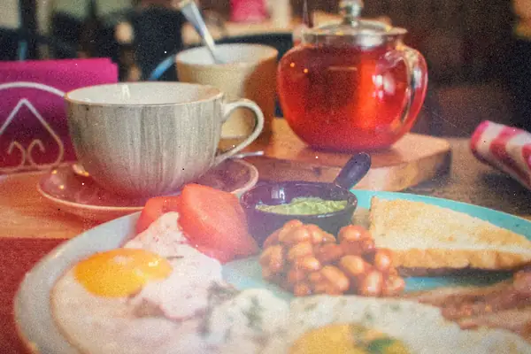A breakfast of fried eggs, bacon, beans, toast and tomatoes beside a teapot and teacup.
