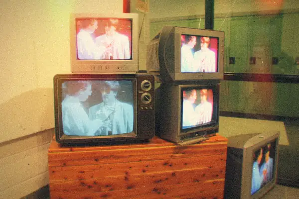 A stack of vintage CRT televisions on a wooden stand, all showing the same old program.