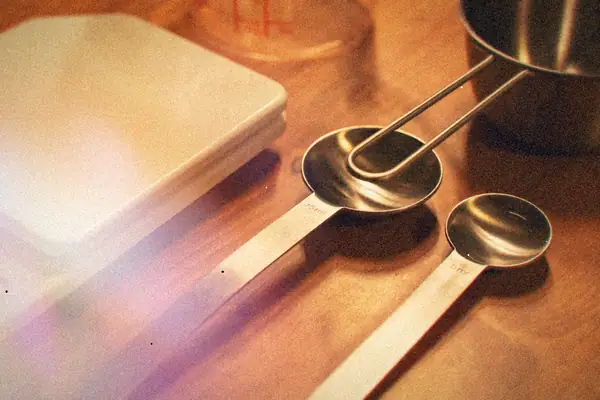 Metal measuring spoons, a measuring cup, a glass measuring jug and a kitchen scale on a wooden counter.