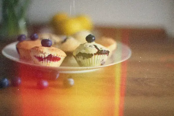 A plate of small blueberry muffins topped with blueberries, with lemons blurred in the background.