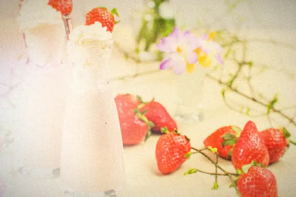 Two strawberry shakes topped with whipped cream and whole strawberries, with more berries on the table.