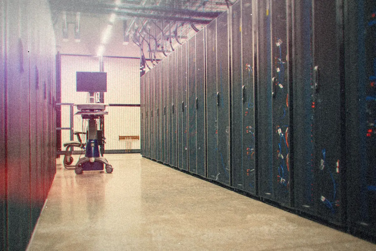 A long aisle of dark server racks in a data center, with a monitor cart at the far end.