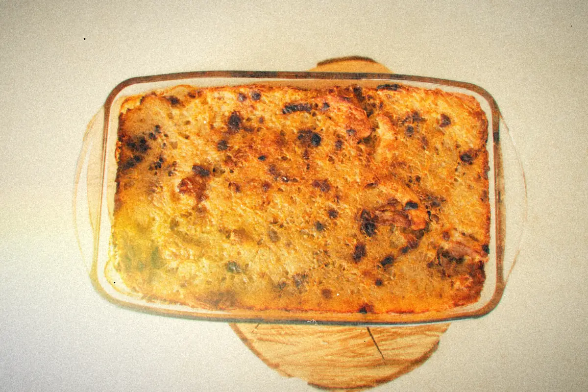 A golden baked casserole in a glass baking dish set on a wooden board.