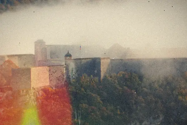 An old stone fortress on a hillside half swallowed by fog above autumn trees.
