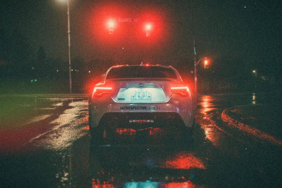 A car waiting at a red light on a wet city street at night.