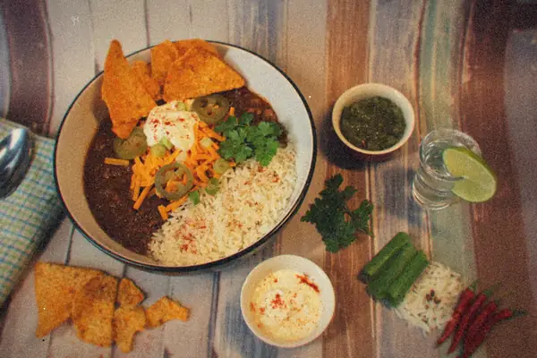 A bowl of rice and seasoned beef topped with cheddar, sour cream, jalapeños and cilantro, with tortilla chips on the side.
