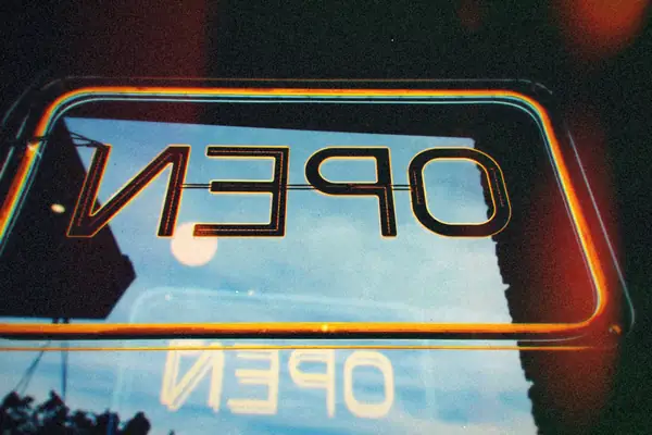 A neon open sign hanging upside down in a shop window at night.
