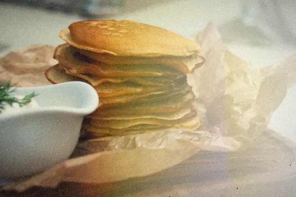 A homemade stack of pancakes on parchment on a rustic wooden board.