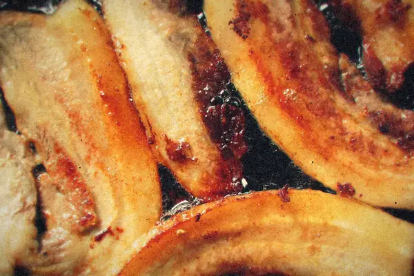 Thick strips of bacon sizzling and browning in a frying pan.
