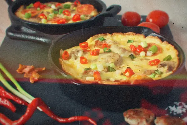 Two cast iron skillets of frittata topped with sausage, tomato, chili and green onion.