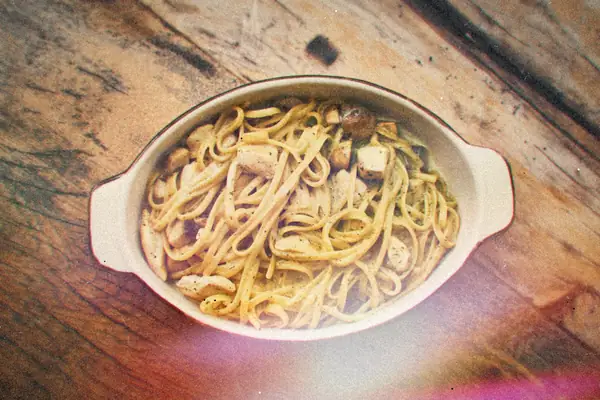 Linguine with chicken and mushrooms in an oval white baking dish on a wooden table.