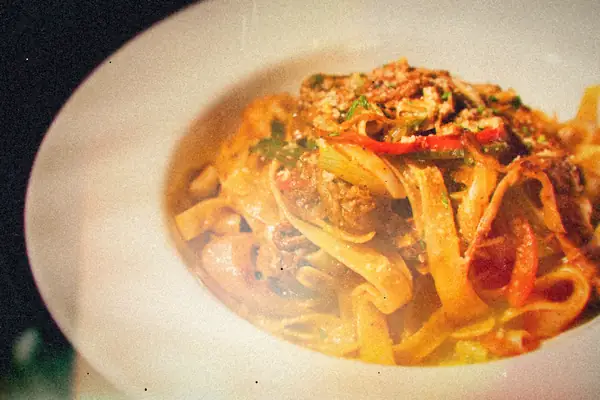 A white bowl of tagliatelle tossed with shredded beef, red peppers and green onion.