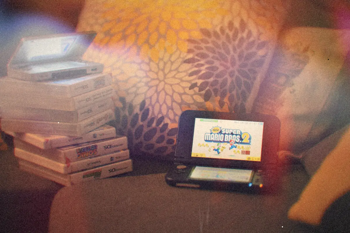 A stack of Nintendo DS game cases on a sofa with a silver DS on top and a 3DS XL beside them.