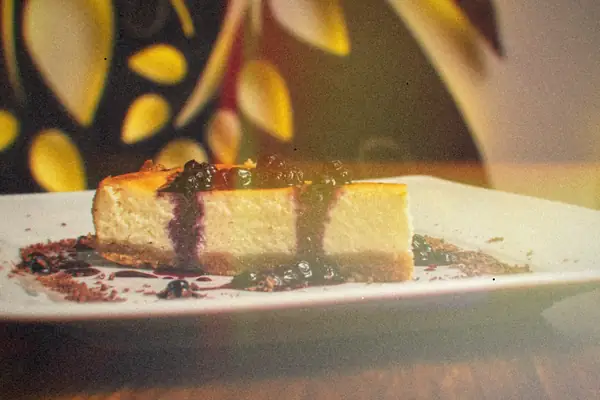 A slice of cheesecake topped with blueberries and blueberry sauce on a white plate.