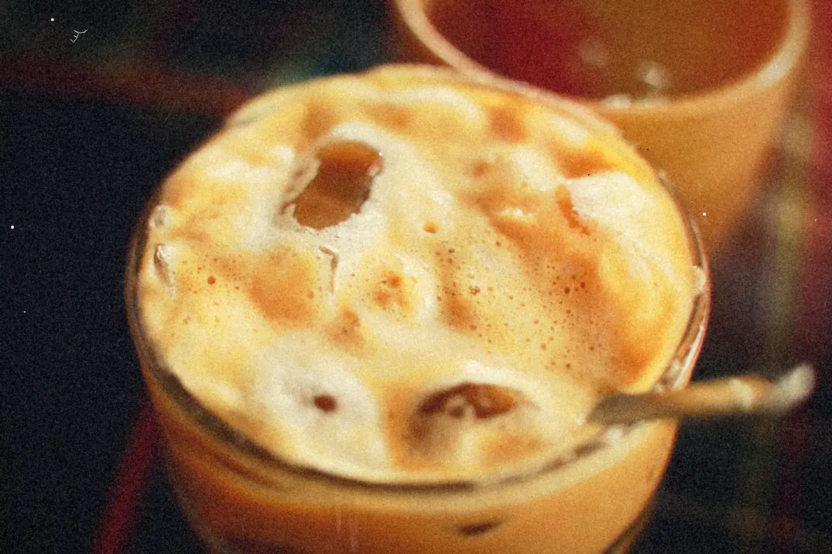 A close-up of iced coffee in a glass topped with thick creamy foam.
