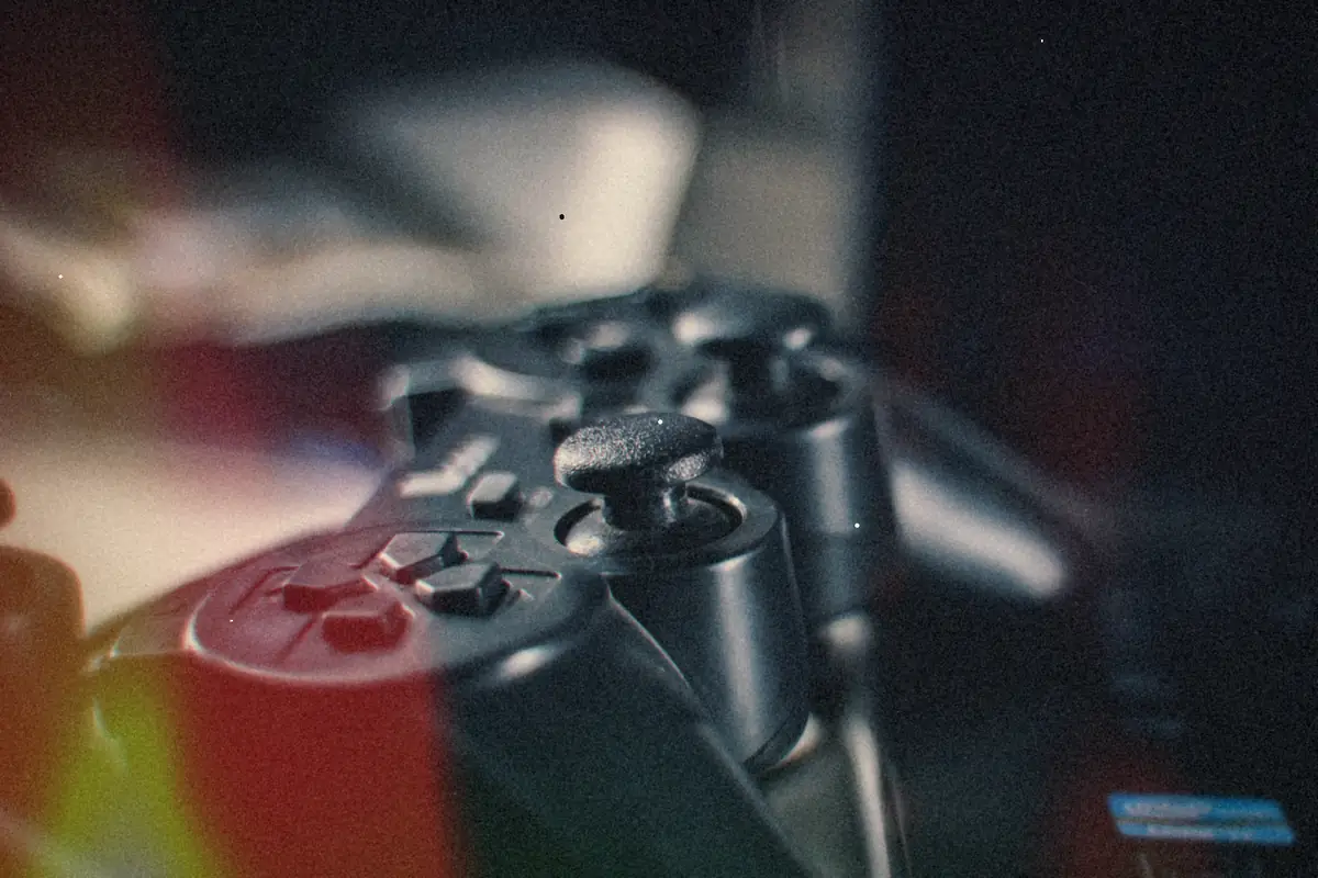 A pair of black PlayStation 3-style controllers in low light, one resting on top of the other.