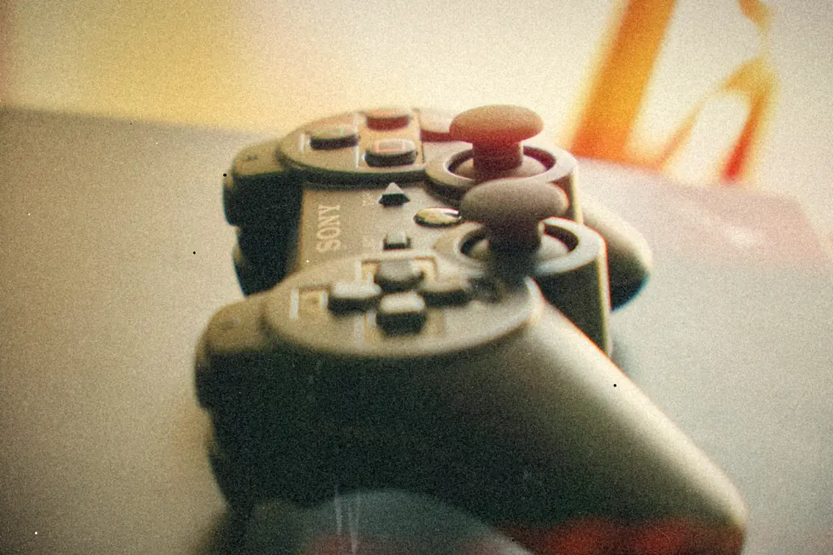 Two black PlayStation 3 controllers stacked on a dark surface, shot close with a soft background.