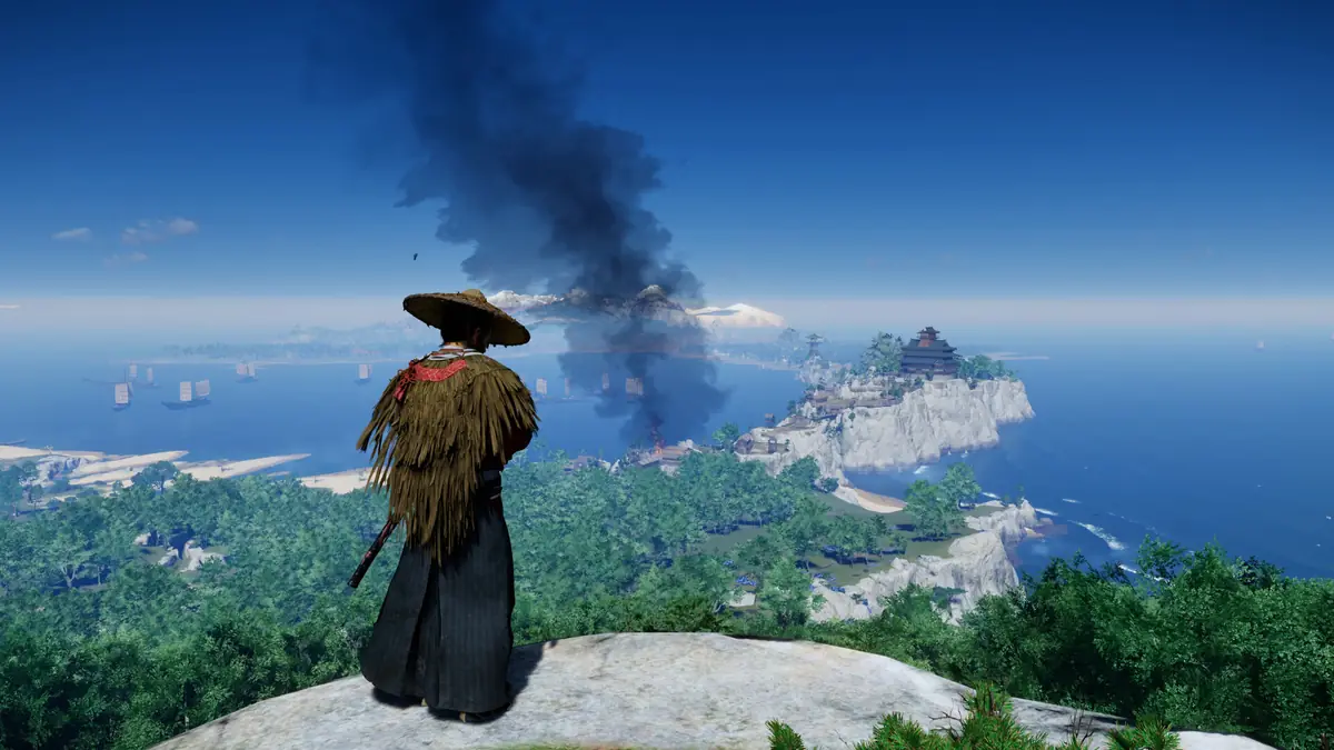 A lone samurai standing on a cliff above a coastline as smoke rises from a distant village in Ghost of Tsushima.