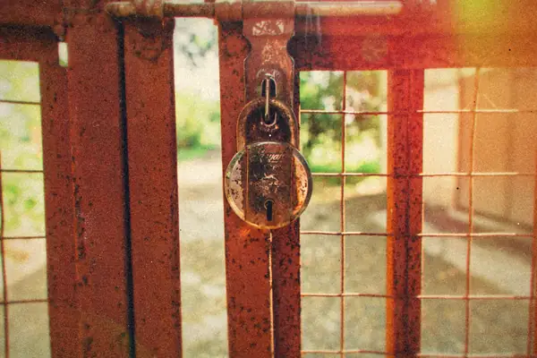 A rusty padlock hanging on a weathered metal gate.
