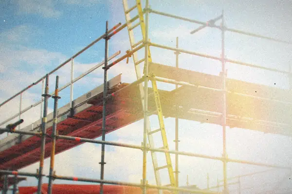 Metal scaffolding and a yellow ladder against a blue sky.