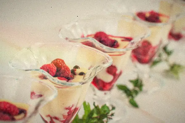 Glass dessert cups of creamy pudding layered with raspberry sauce and topped with fresh raspberries.