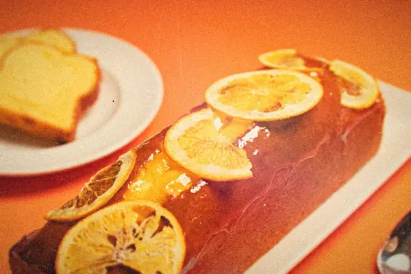 A glazed citrus loaf cake topped with candied citrus slices, with cut slices on a plate behind it.