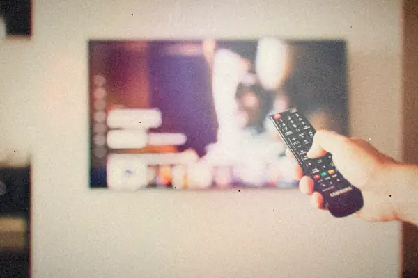 A hand pointing a remote control at a TV showing a streaming menu.