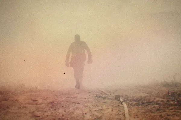 A lone soldier's silhouette walking through thick smoke.
