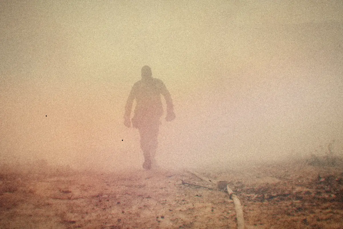 A lone soldier's silhouette walking through thick smoke.