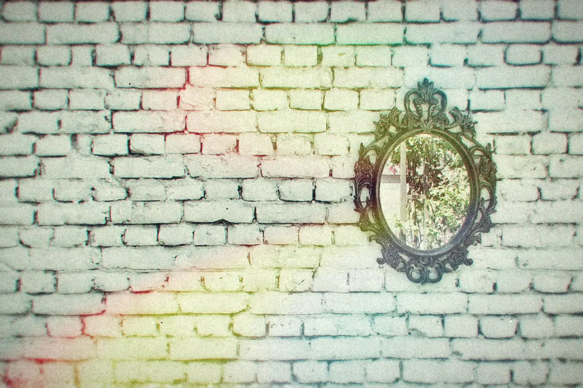 A small ornate mirror hanging alone on a pale painted brick wall.