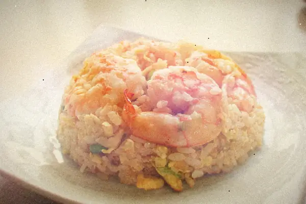 A mound of egg fried rice with scallions topped with pink shrimp on a white plate.