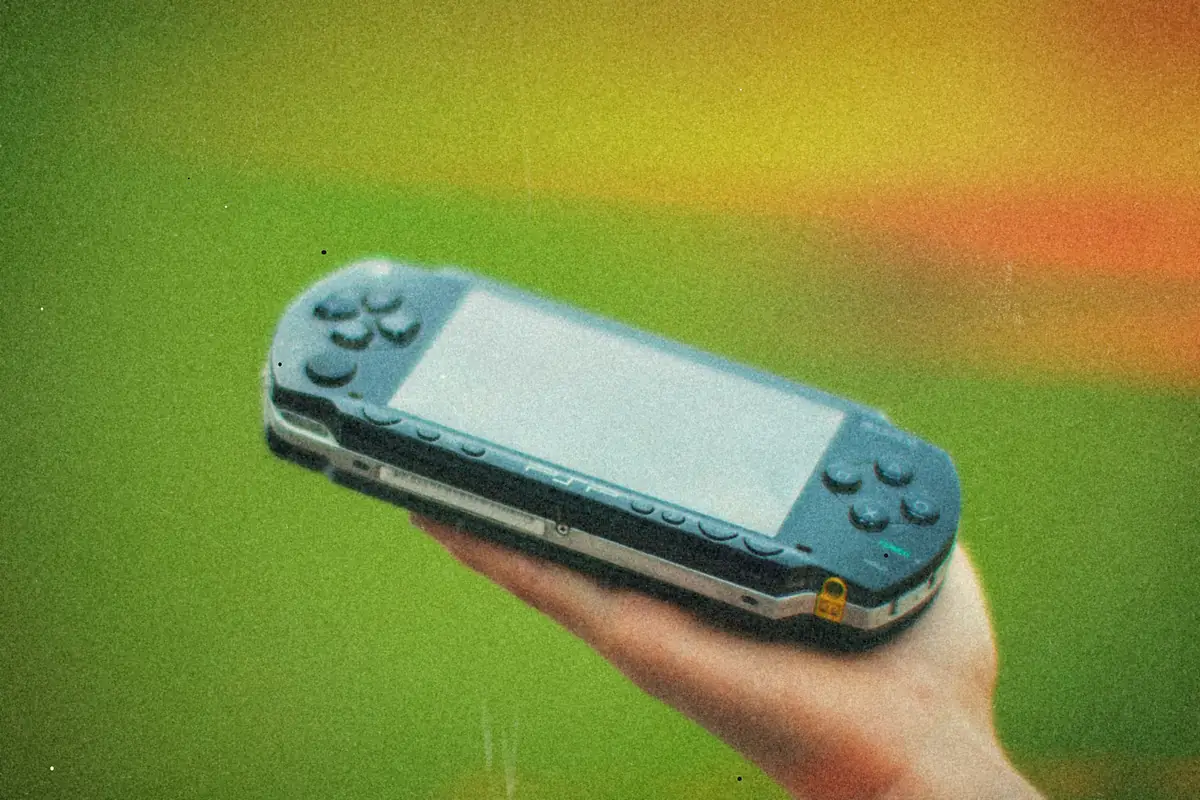 A hand holding up a black PSP against a blurred green background.