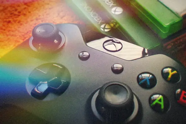A stack of green video game cases behind a black controller resting on an orange carpet.