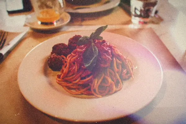 A plate of spaghetti in tomato sauce with meatballs and a sprig of fresh basil.