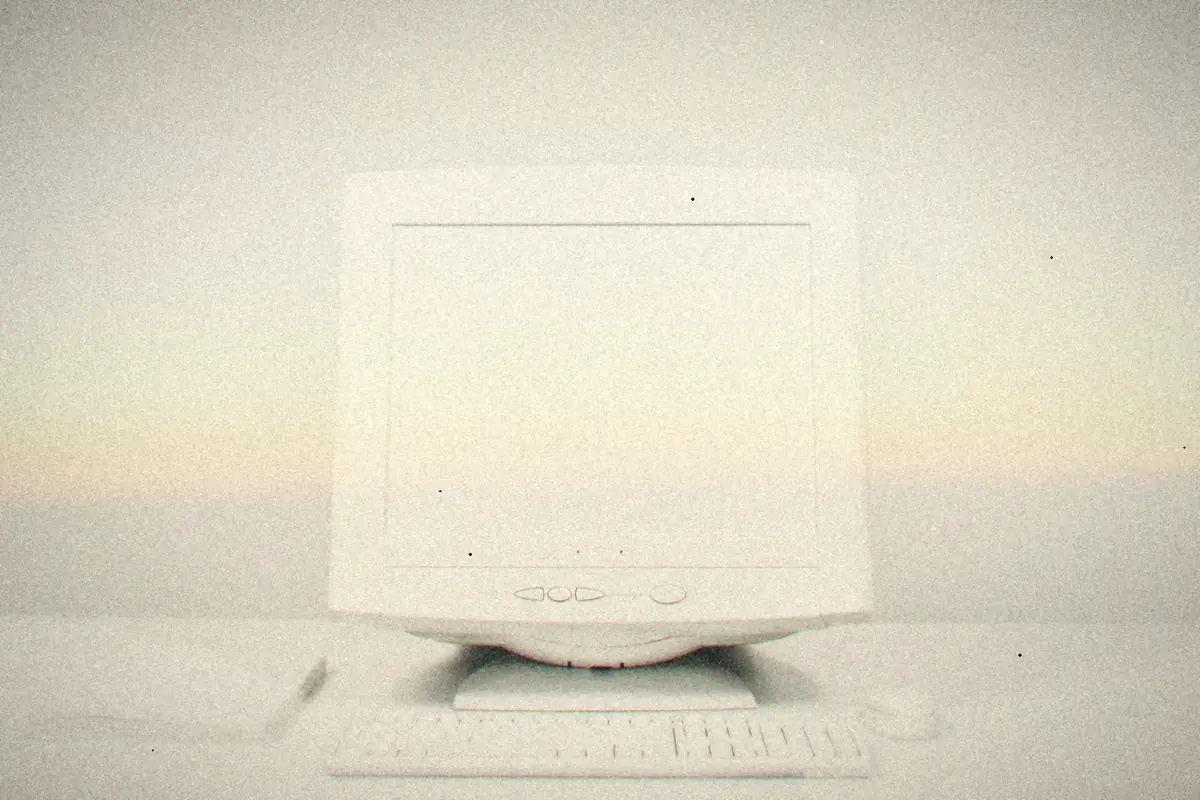 A late-'90s white CRT monitor with a matching keyboard and mouse on a plain white desk.