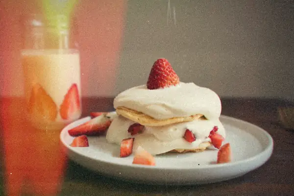 A strawberry shortcake layered with whipped cream and fresh strawberries on a white plate.